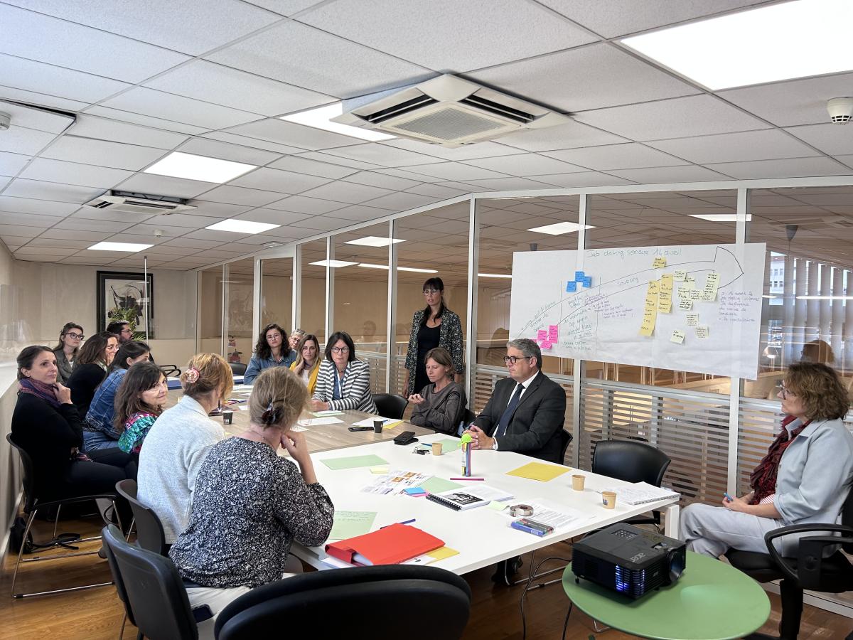 Plusieurs personnes sont assises autour d'une grande table et semblent échanger.