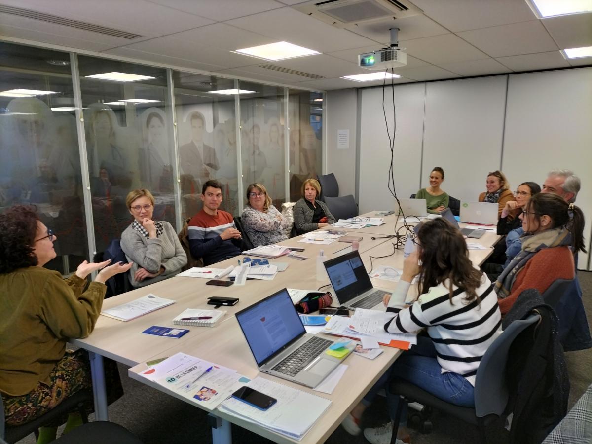 Une dizaine de personnes échangent autour d'une table sur laquelle sont posés divers papiers et ordinateurs.