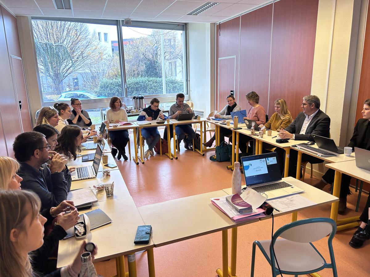 Une vingtaine de personnes sont assises autour d'une table disposée en U